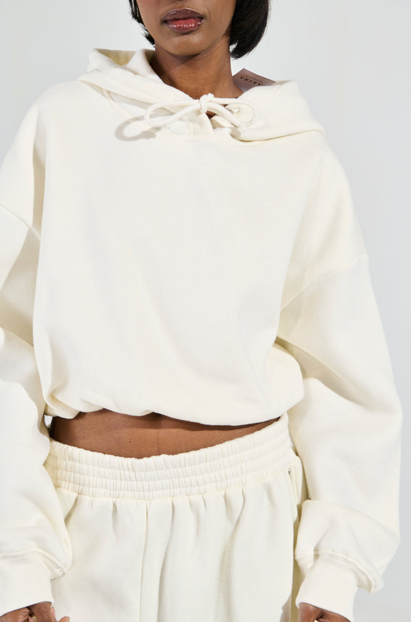The individual is sporting the AINT NOBODY SWEATSHIRT IN CREAM, an oversized hooded cotton-blend piece with a drawstring, complemented by matching sweatpants. The ensemble radiates a soft and comfortable aura ideal for casual loungewear.
