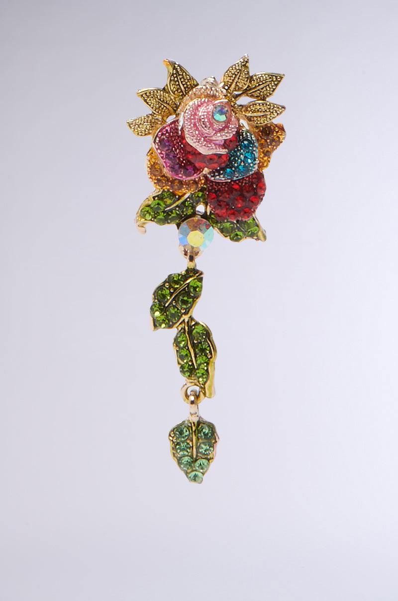 The SUMMER GARDEN DANGLE EARRING showcases a vibrant rose design with rhinestone-adorned leaves. It features pink, red, green, and gold shimmering stones and intricate details with a dangling leafy stem against a plain backdrop. 2