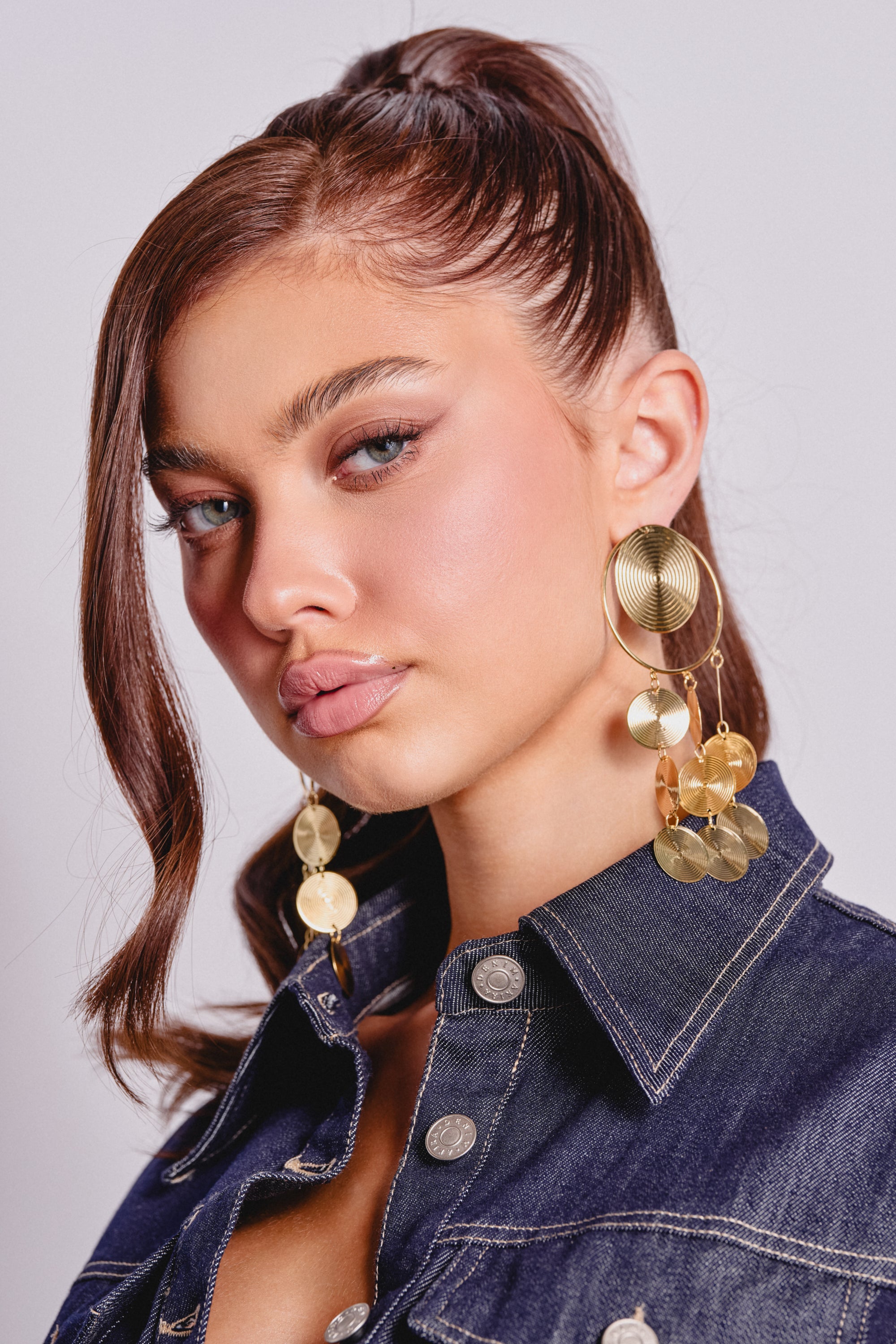 A young woman with brown hair pulled back wears the striking TAKE ME AWAY EARRING and a dark denim jacket. 2