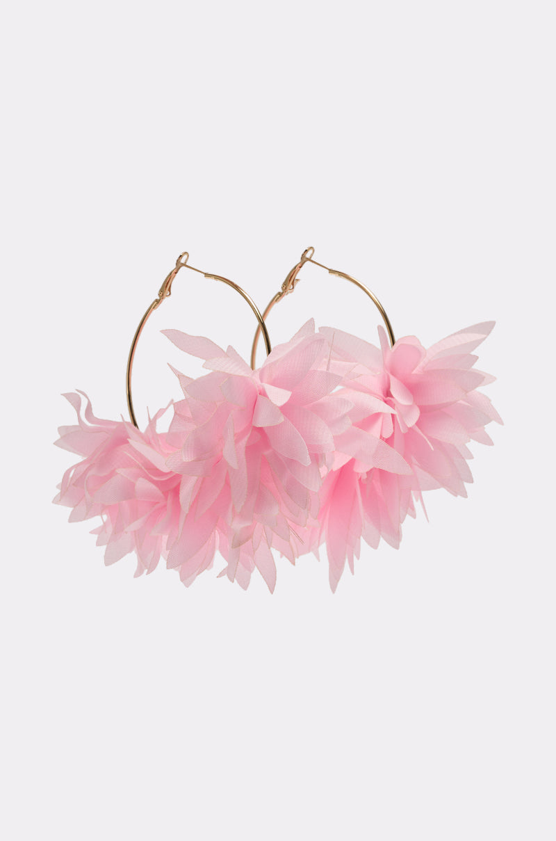 The WINDSWEPT EARRING features gold floral hoops adorned with large, light pink fabric flowers, creating a whimsical statement piece. Displayed on a plain white background. 0