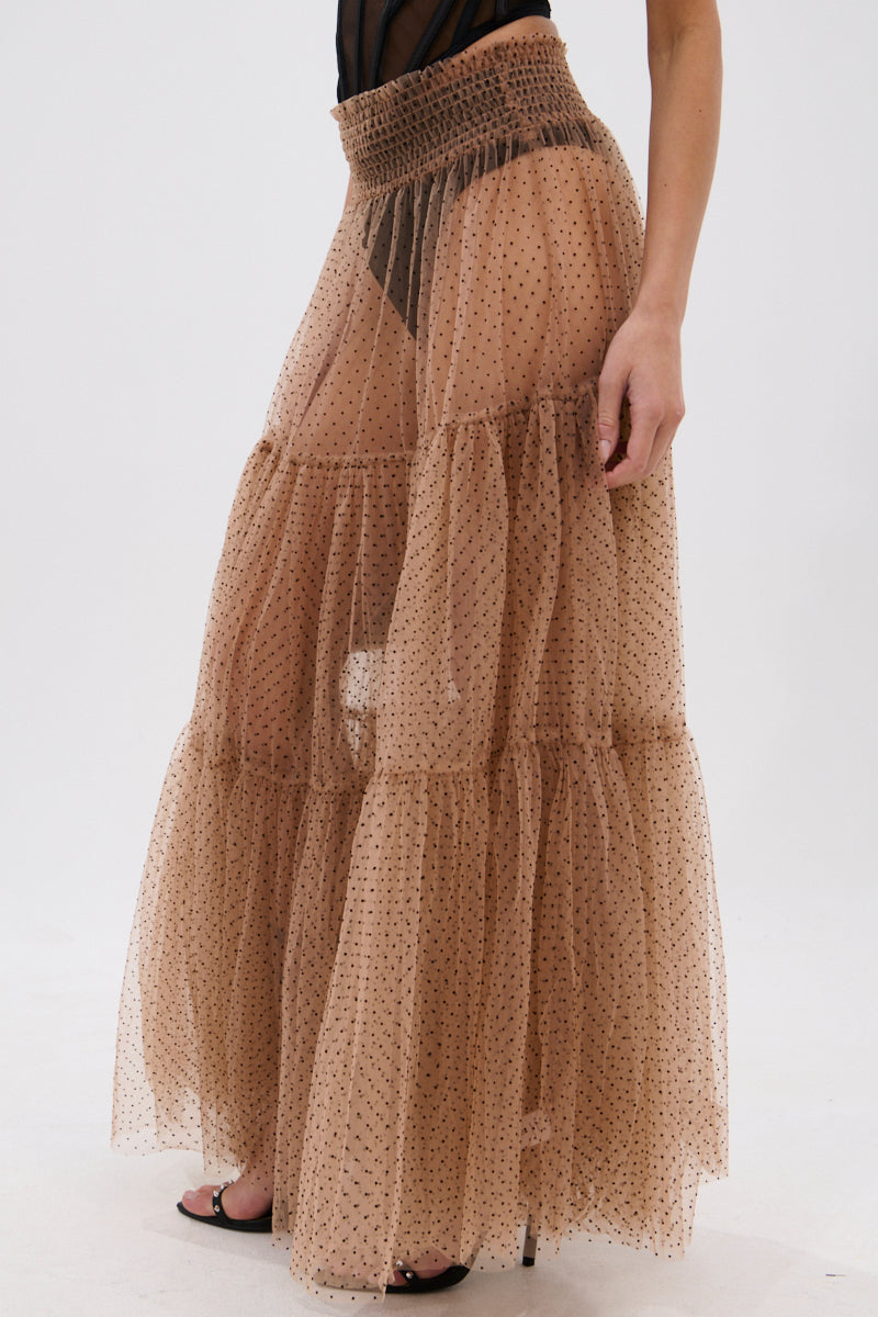 Wearing the CLASSY POLKA DOT MAXI SKIRT—a high-waisted, sheer, layered organza maxi with small black polka dots—paired with a black top and heeled sandals. The light brown skirt’s semi-transparent design adds elegance. 3