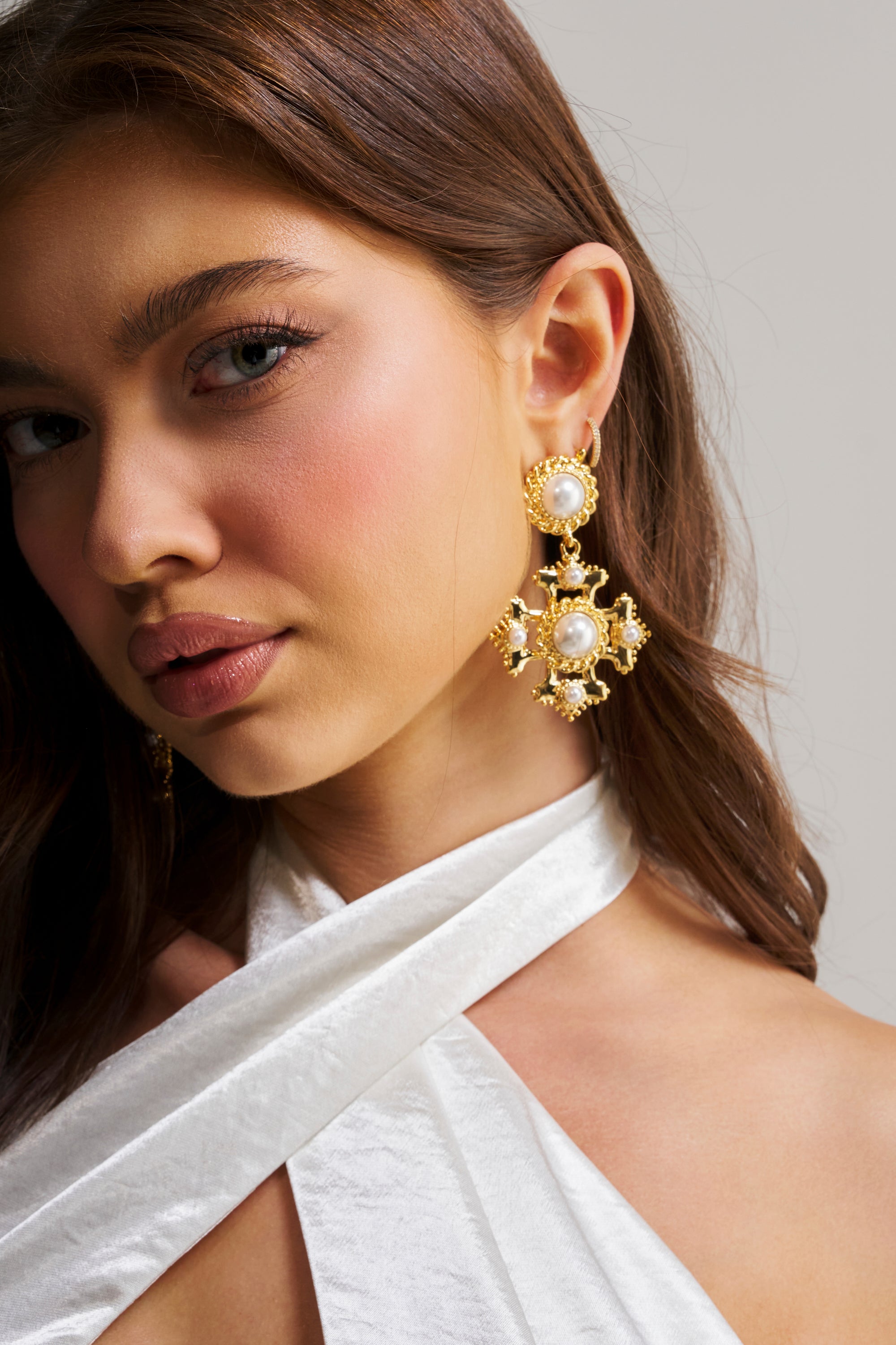 A woman with long brown hair wears a white halter top and the IN YOUR DREAMS EARRING, gazing slightly to the side against a neutral background.