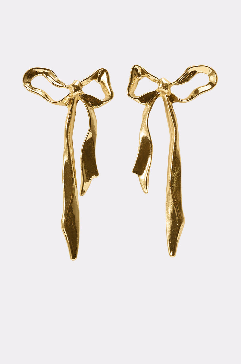 The TIE IT WITH A BOW EARRING features shiny coquette bow-shaped earrings with long, flowing ribbon tails, set against a plain light gray background. 1