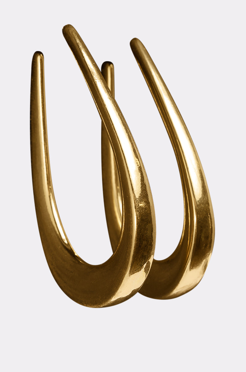 The BELLE EARRING features a shiny, gold-tone finish and crescent shape with smooth, curved surfaces, standing upright against a plain light background. 2