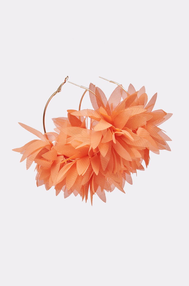 The FOR THE SUMMER EARRING is a pair of oversized hoop earrings featuring layered orange fabric petals shaped like large flowers, displayed against a plain light background. 0