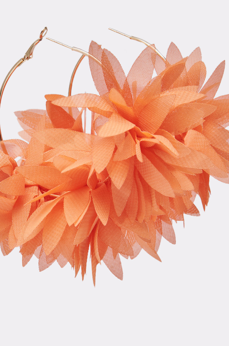 Close-up of FOR THE SUMMER EARRING: oversized gold-tone hoops embellished with bold, layered orange fabric petals shaped like flowers. Shown against a simple, light background. 4