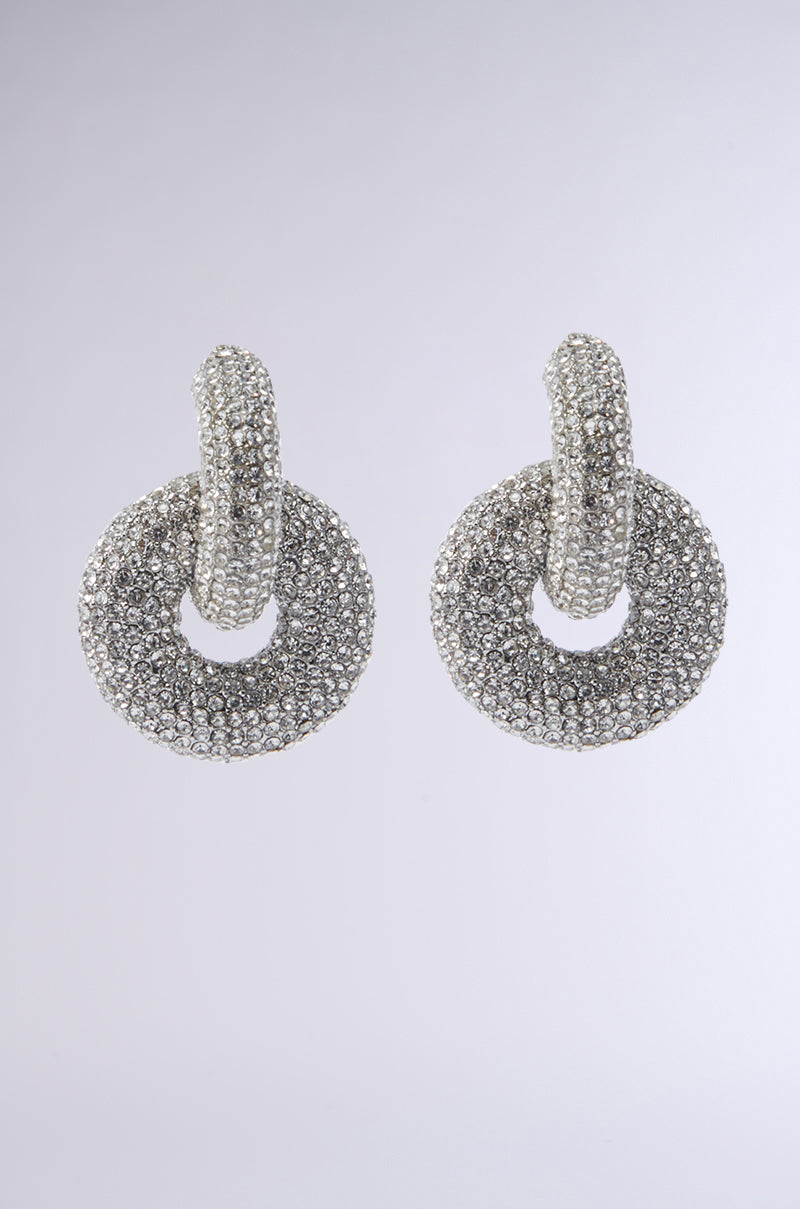 LUXURY EARRING: Silver circular earrings featuring a textured design and rhinestone embellishments at the looped top section, set against a light gray background.