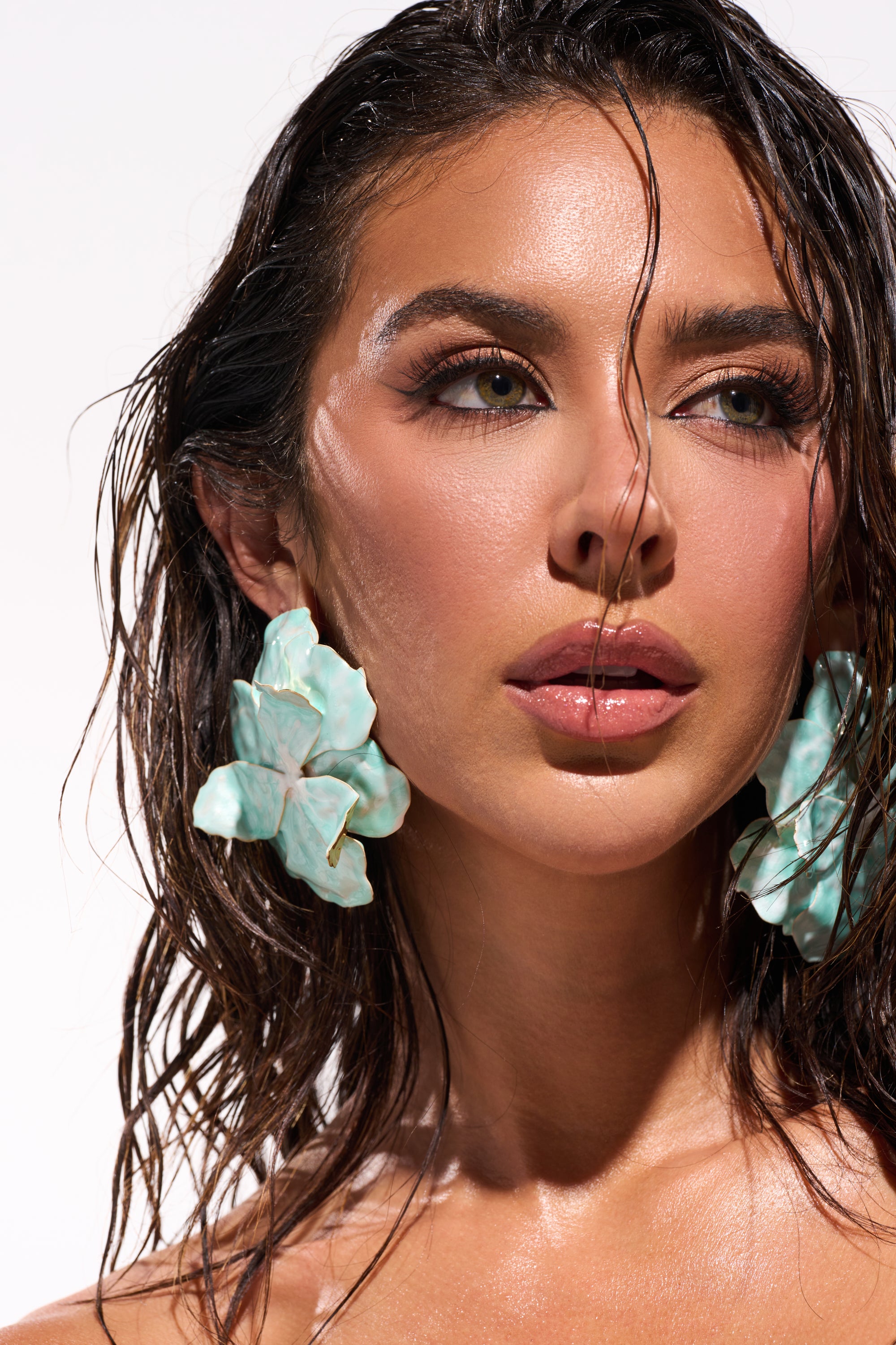 A woman with wet, wavy hair poses against a light background, wearing FLOWER POWER BLUE EARRING. Her dewy makeup features glossy lips and defined eyes.