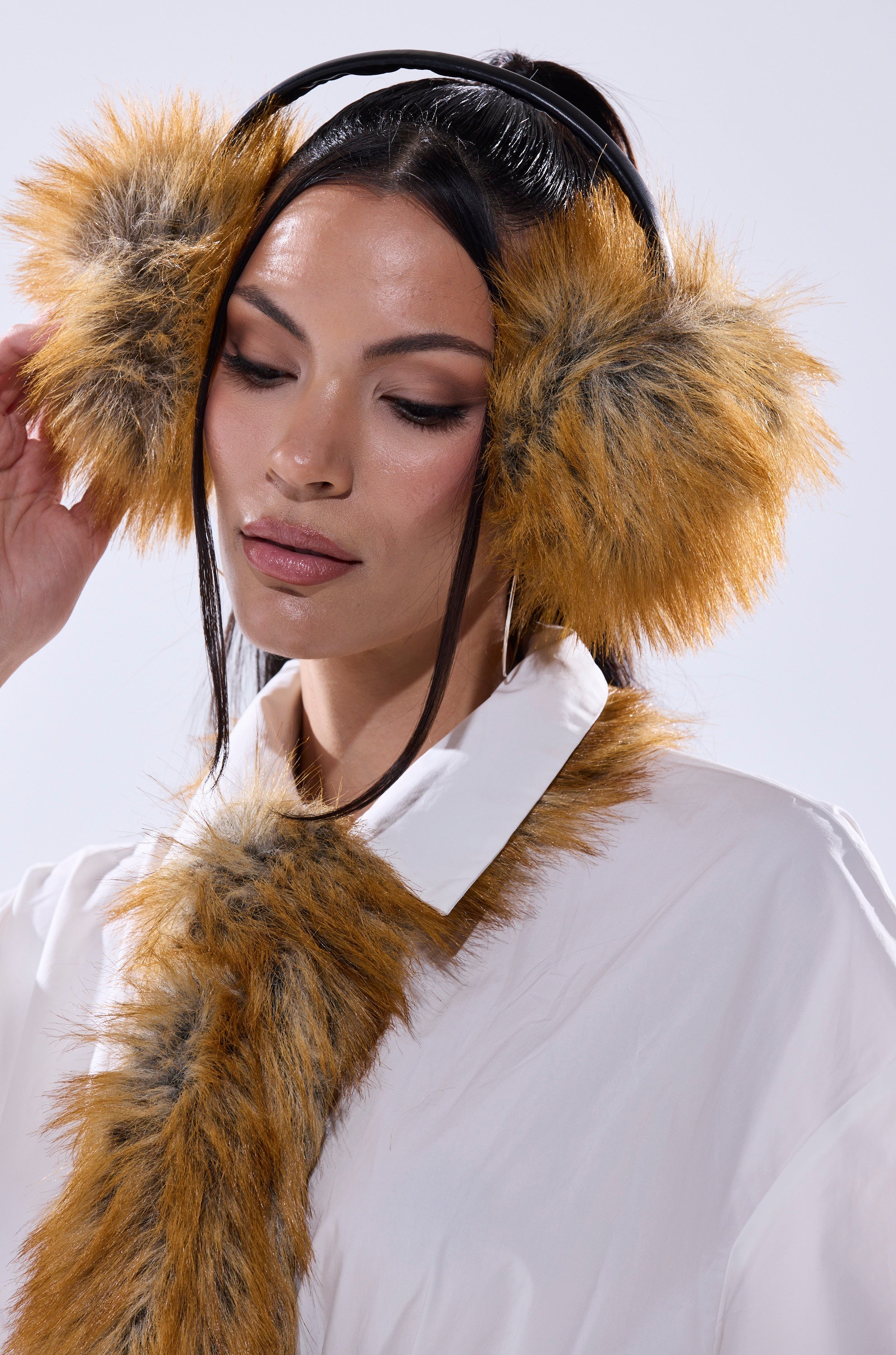 A woman models the REALLY LIKE THAT FAUX FUR EARMUFFS with a matching faux fur scarf over a white shirt, gently touching the earmuffs and tilting her head down—showcasing these elegant cold weather accessories. 5