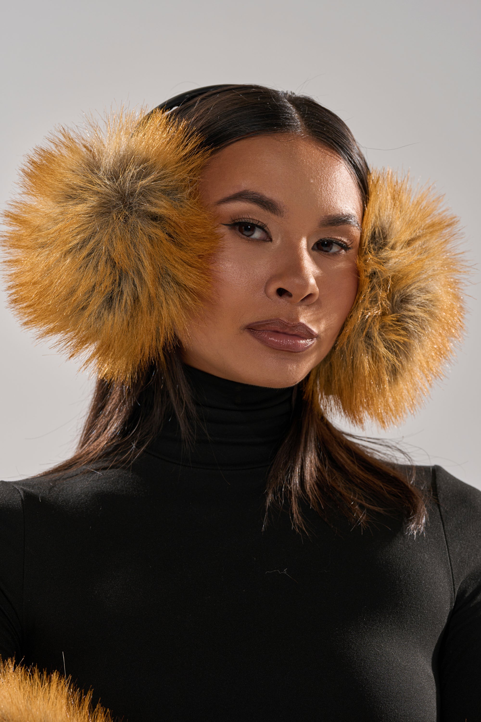 A woman in a black turtleneck wears REALLY LIKE THAT FAUX FUR EARMUFFS and looks at the camera against a plain, light background. 2