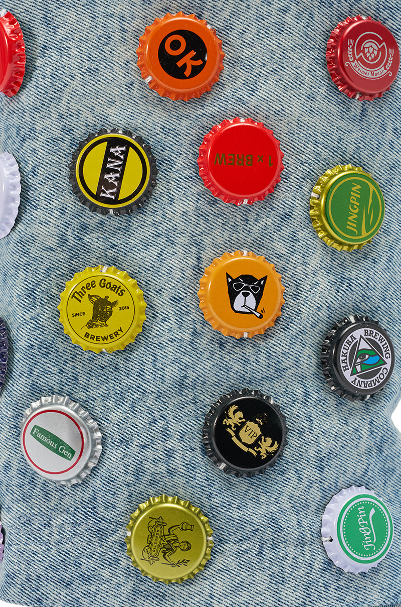 A cluster of bottle caps sits on denim, capturing the playful spirit of the AZALEA WANG EAVEN WEDGE EMBELLISHED DENIM BOOTIE.