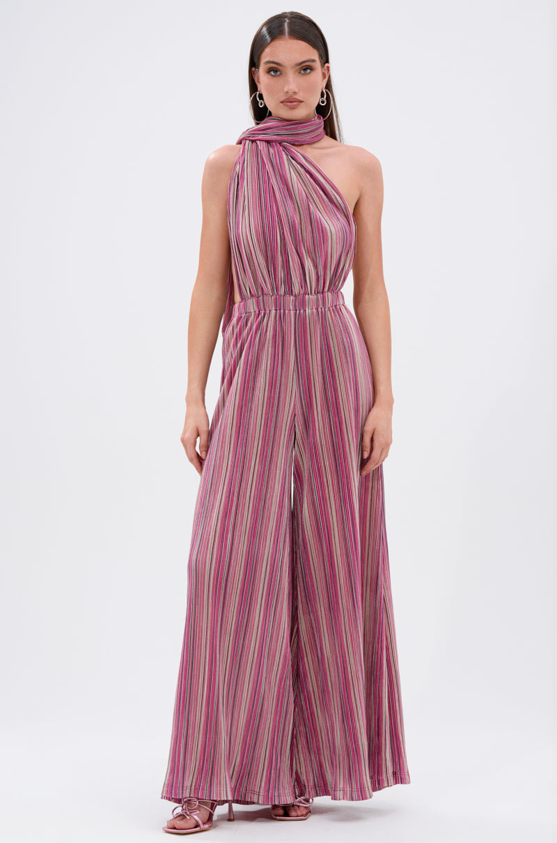 A woman faces forward wearing the JUMPIN AROUND SLINKY JUMPSUIT, a sleeveless halter-neck piece with wide legs and pink, purple, and white vertical stripes, styled with pink heels for a vibrant look. 1