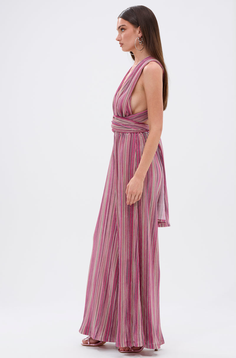 Woman models the JUMPIN AROUND SLINKY JUMPSUIT, a sleeveless, wide-leg jumpsuit with pink, purple, and white vertical stripes, deep V-neck, open sides, and wraparound waist tie; photographed in profile against a white background. 8