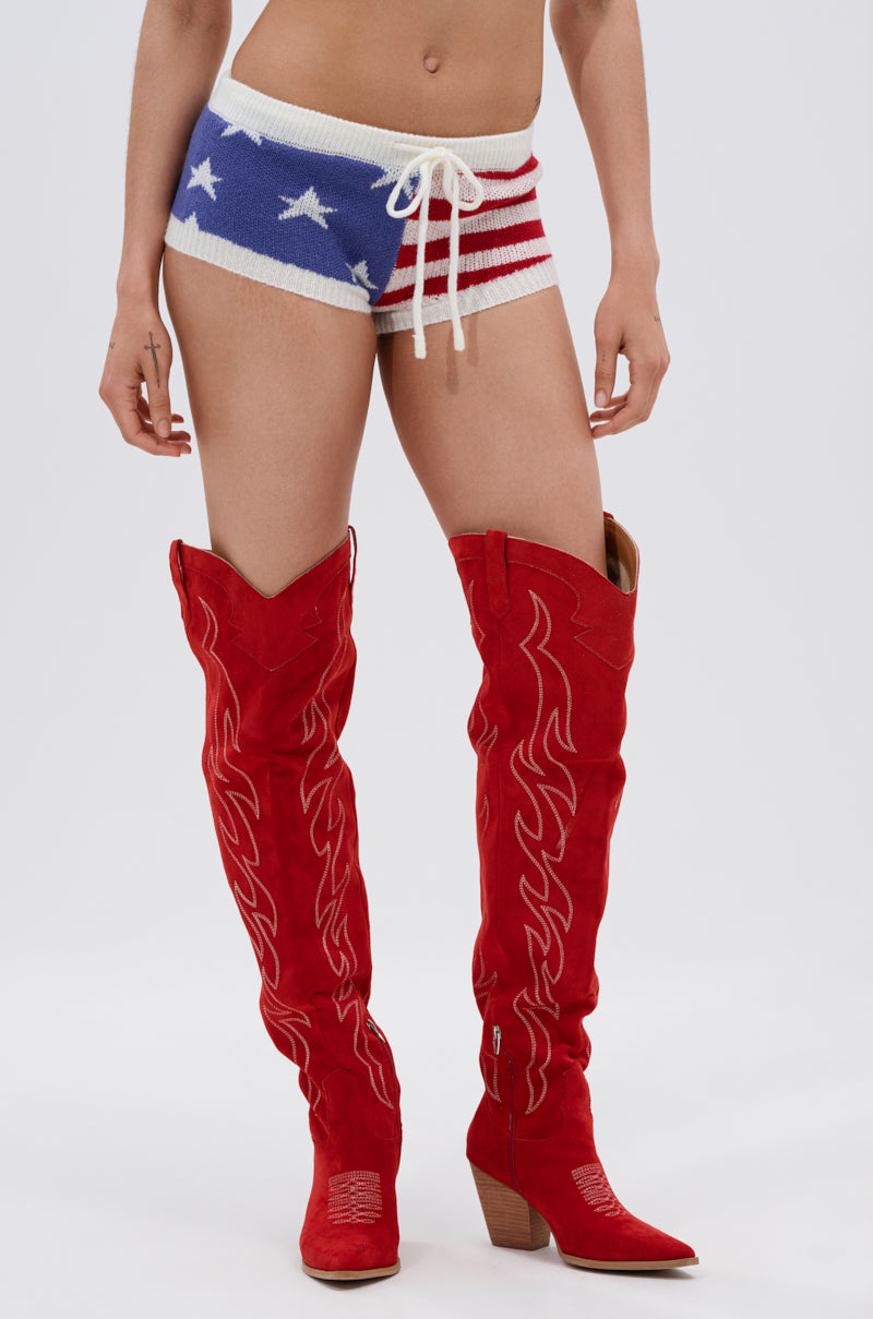 A person wearing the PARTY IN THE USA SHORT, inspired by patriotism with stars and stripes, stands in red cowboy boots with white stitching against a plain white background. Only the lower half is visible.