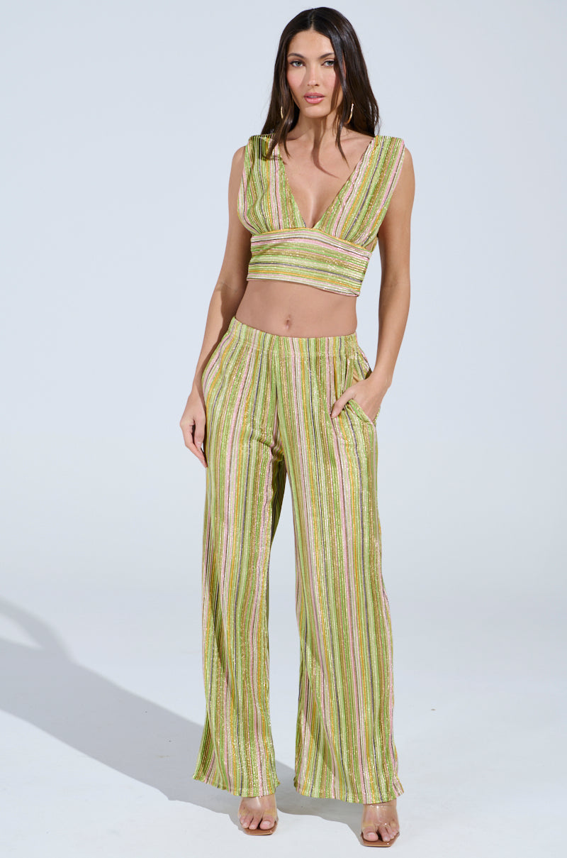 A woman poses in a sleeveless, V-neck crop top with multicolored stripes in green, yellow, and pink alongside high-rise MIXED EMOTIONS PALAZZO PANT. Her hands rest in the pants' pockets, and she wears open-toed shoes against a plain, light-colored background.