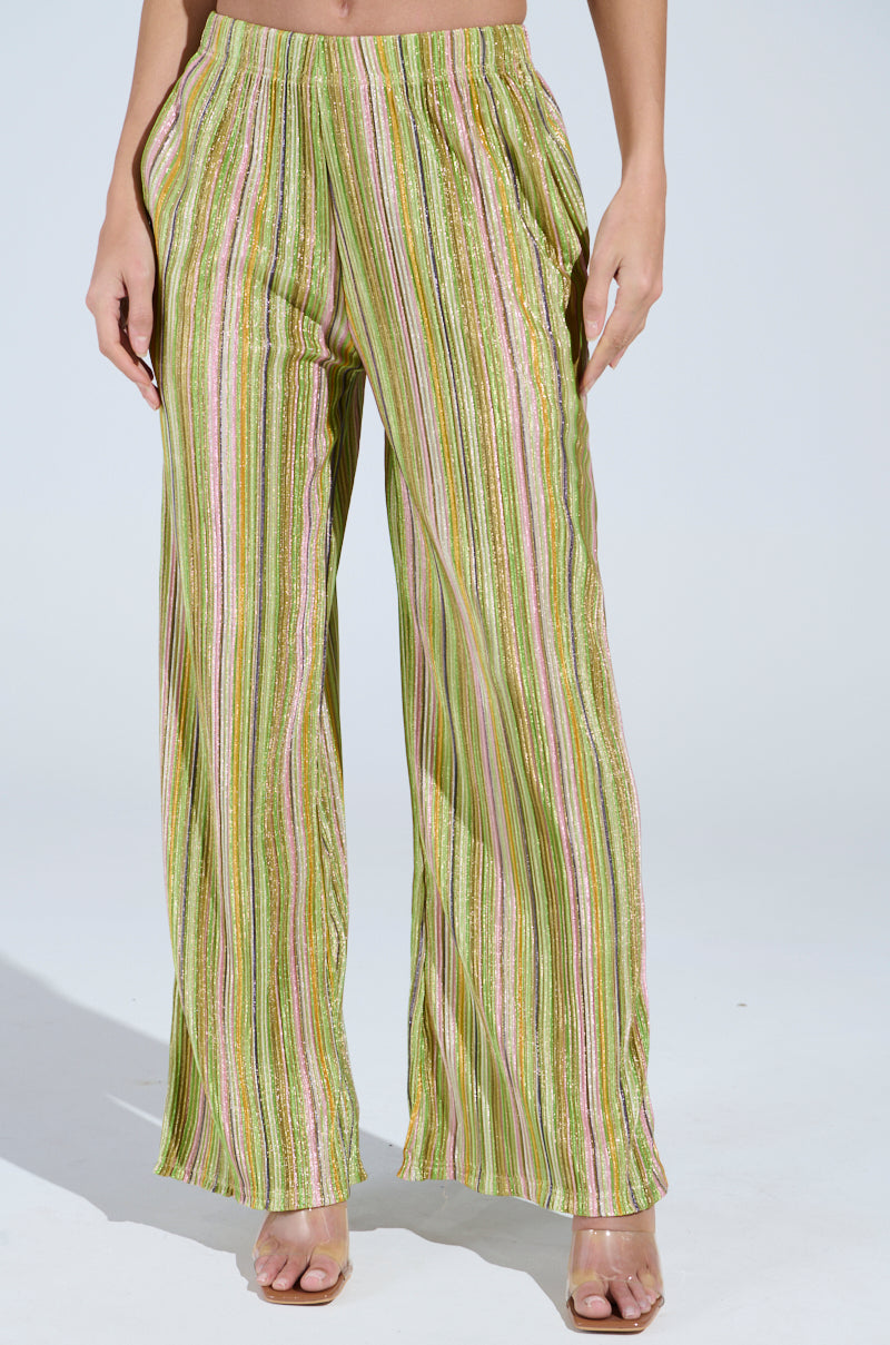 The image showcases a person in the MIXED EMOTIONS PALAZZO PANT, boasting a high-rise cut with multicolored stripes in green, pink, and beige. The shiny textured fabric exudes elegance, paired stylishly with open-toed heels against a simple white backdrop.