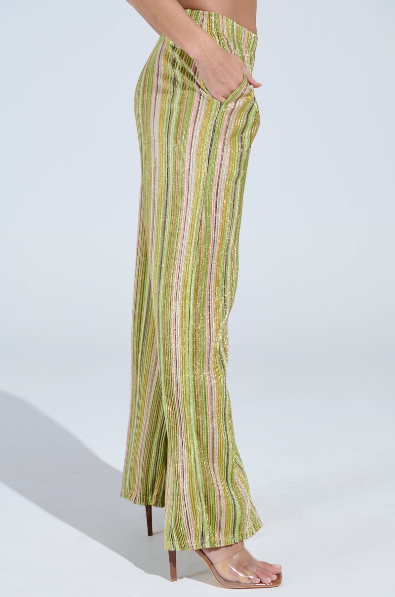 Side view of a person in MIXED EMOTIONS PALAZZO PANT with high-rise, multicolored stripes and flared legs, paired with transparent high heels against a plain, light-colored background.