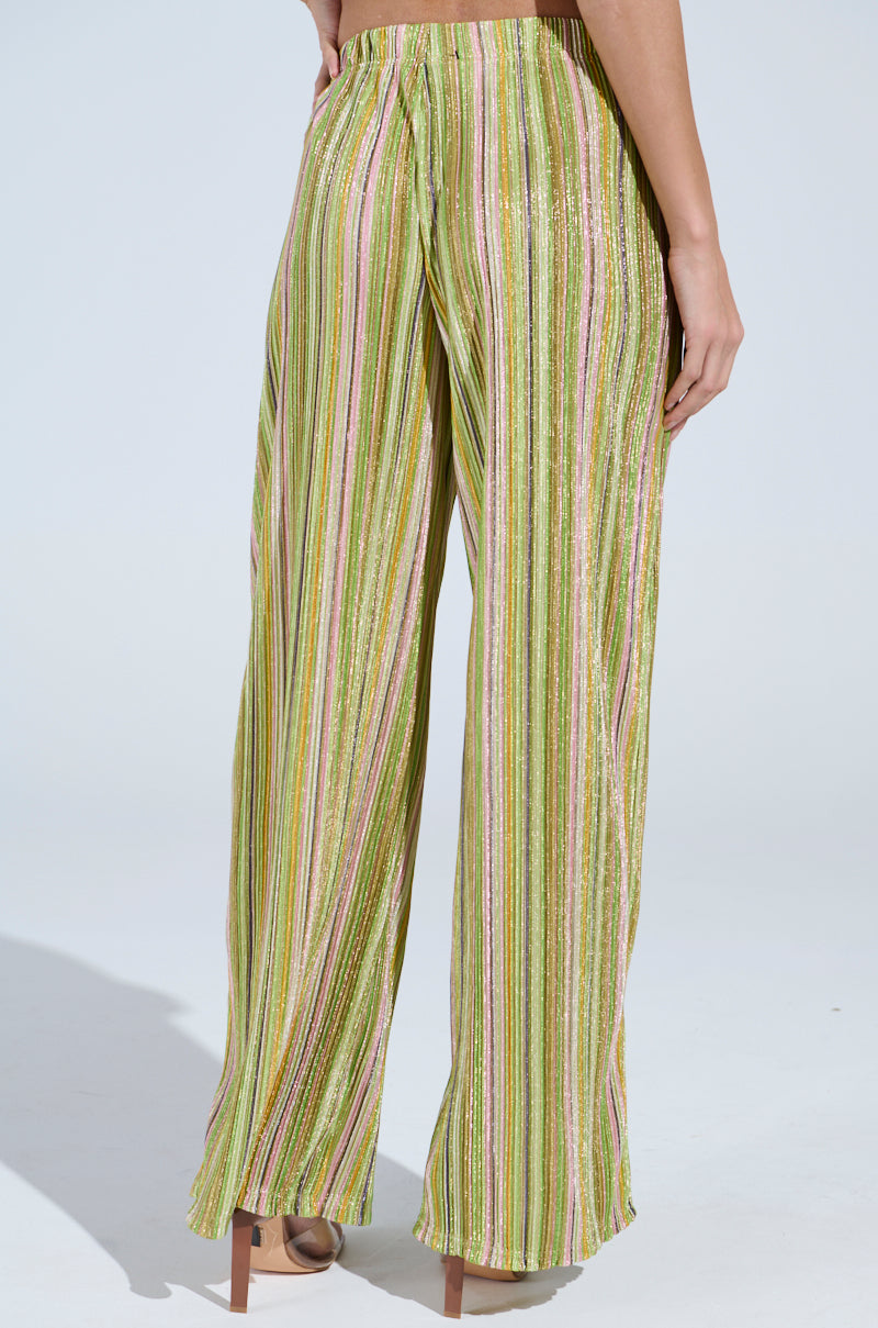 Someone showcases the elegant MIXED EMOTIONS PALAZZO PANT, featuring a multicolored stripe pattern in greens, pinks, and gold. The shimmering wide-leg design pairs perfectly with their barefoot pose against a plain light background.