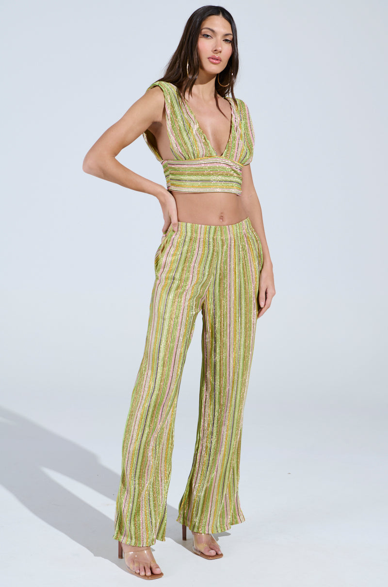 A person stands confidently in a fashionable lime green ensemble featuring a sleeveless crop top and the MIXED EMOTIONS PALAZZO PANT with a multicolored stripe pattern. High-heeled sandals, long hair, and hoop earrings complete the chic look.