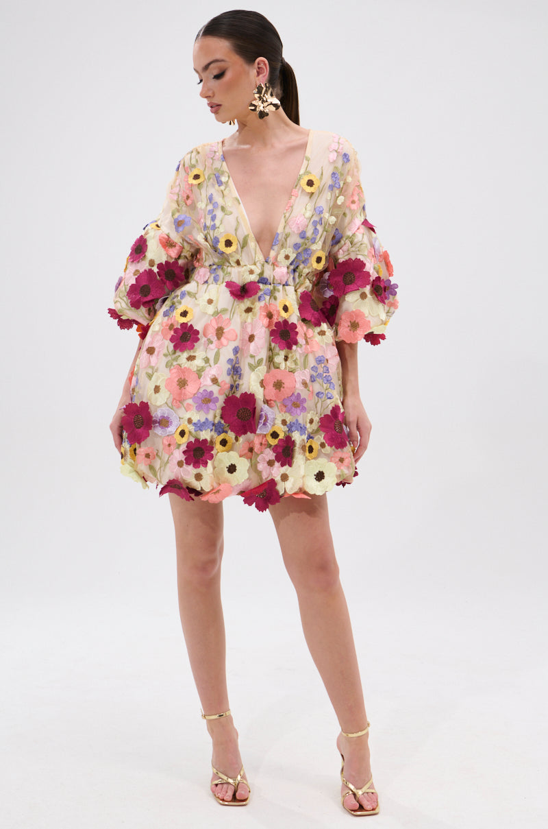 Woman modeling the FLORAL BABY MINI DRESS—a short, sheer mini dress with colorful 3D floral embroidery, voluminous sleeves, and deep V neckline—paired with gold high-heeled sandals against a plain white background. 6