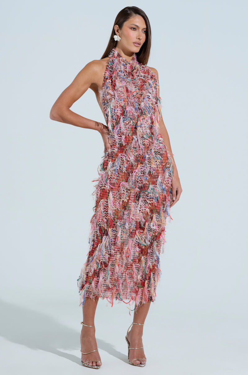 A woman poses confidently in the curve-hugging Summer Time Livin' Mesh Midi Dress in Pink, featuring a colorful fringe pattern, sleeveless style, against a light background. She pairs it with strappy heels and statement earrings, standing with one hand on her hip.