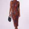 Against a plain backdrop, a woman stands wearing the SUMMER TIME LIVIN MESH MIDI DRESS, featuring a textured, striped color block design in shades of red, blue, and tan. She holds a black clutch in her left hand and wears black lace-up heels. Her hair is pulled back.