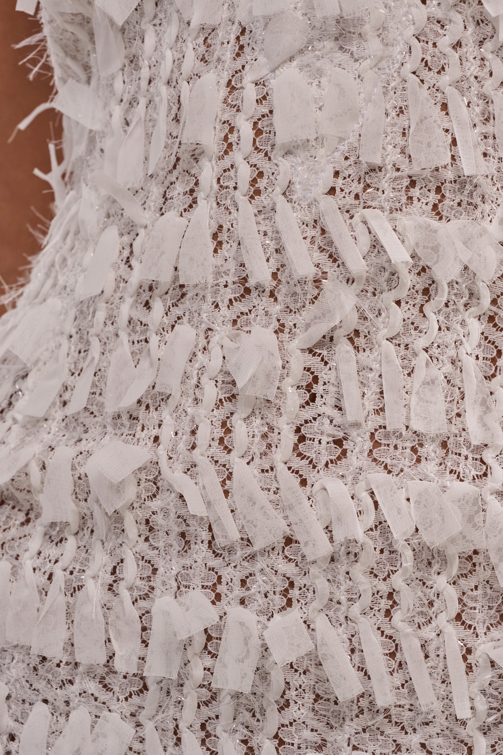 Close-up of the SHAKE IT UP MINI DRESS, showcasing white textured fabric with intricate lace and small, irregular fabric strips sewn throughout for a detailed, bridal-inspired look. 6