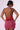 A person is depicted from behind wearing the AKIRA FIREWORKS MINI DRESS, which features a halter neck design and vibrant red and light purple horizontal stripes. They have short, tied-back hair, accessorized with large hoop earrings and sunglasses. The backdrop is plain and light-colored.