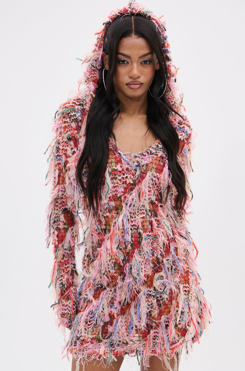 A person wearing the DAYDREAMING FRINGE MINI DRESS WITH A HOOD, featuring vibrant shades of pink, red, and green fringes on a woven fabric with loose threads for a feathered look. The eye-catching dress stands out against a plain white background. 1