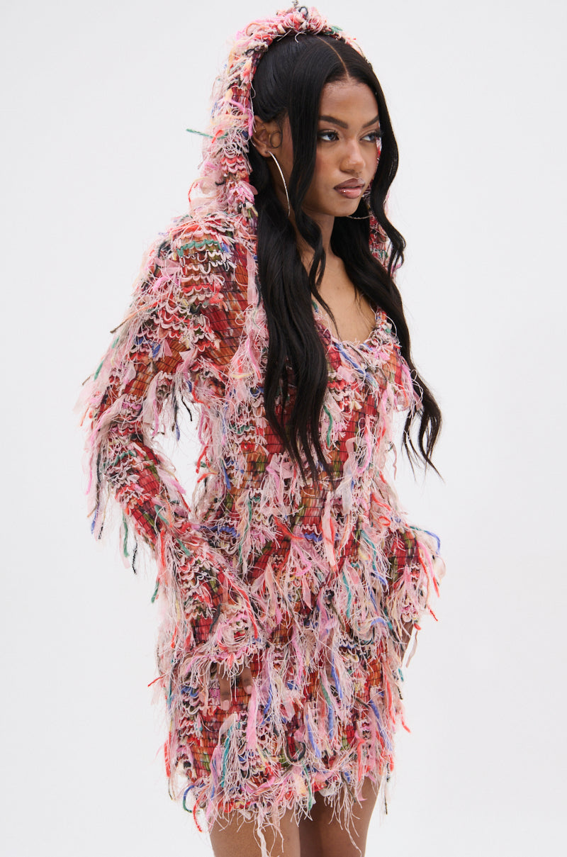 Wearing the DAYDREAMING FRINGE MINI DRESS WITH A HOOD, featuring vibrant multicolored patterns and playful fringe details, a person with long dark hair stands confidently against a plain white background. 2