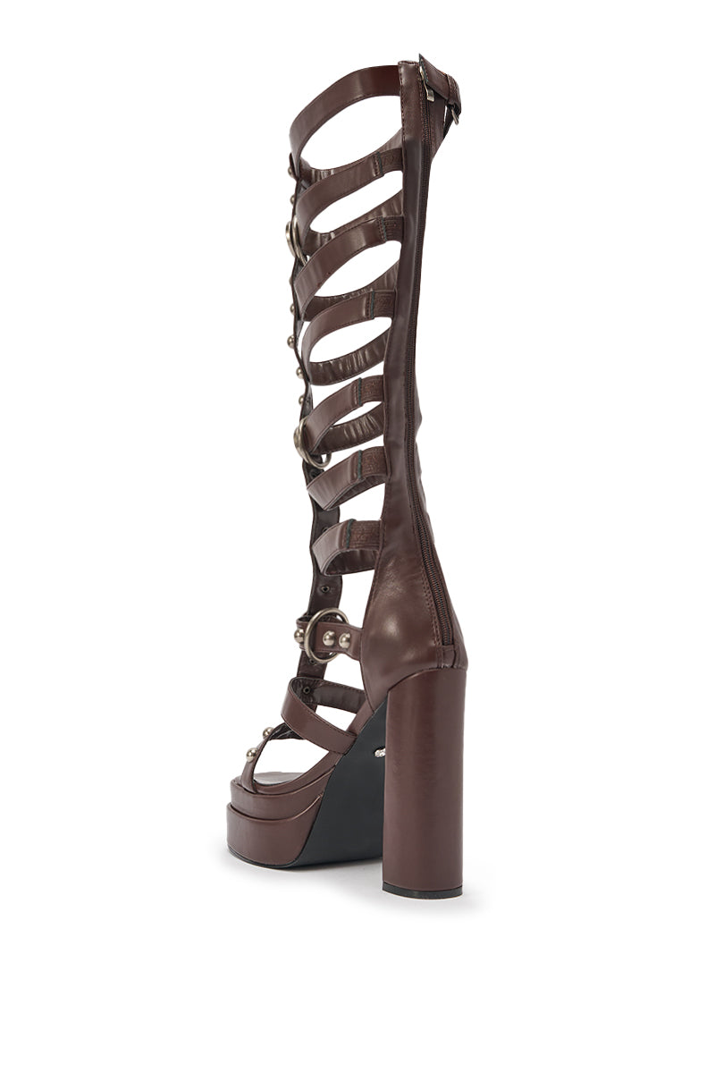 The AKIRA GOLD EDIVA CHOCOLATE GLADIATOR CHUNKY SANDAL is a tall brown knee-high faux leather sandal with multiple horizontal straps, metal buckles, and a platform heel, shown from the side against a white background. 5
