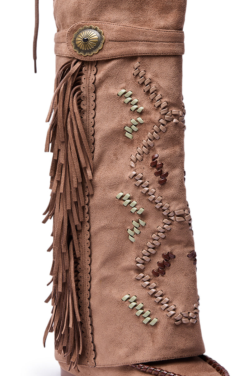 The AZALEA WANG EDMUND BROWN FLAT WESTERN BOOT features tan faux suede, geometric stitching, side fringe accents, scalloped edging, and a round metal concho ornament near the top.