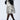 A person wearing a patterned coat with black fur trim on the collar and cuffs, paired with black stockings and the stylish AZALEA WANG EILANA LEOPARD STILETTO PUMP. The light gray background perfectly highlights their striking ensemble.