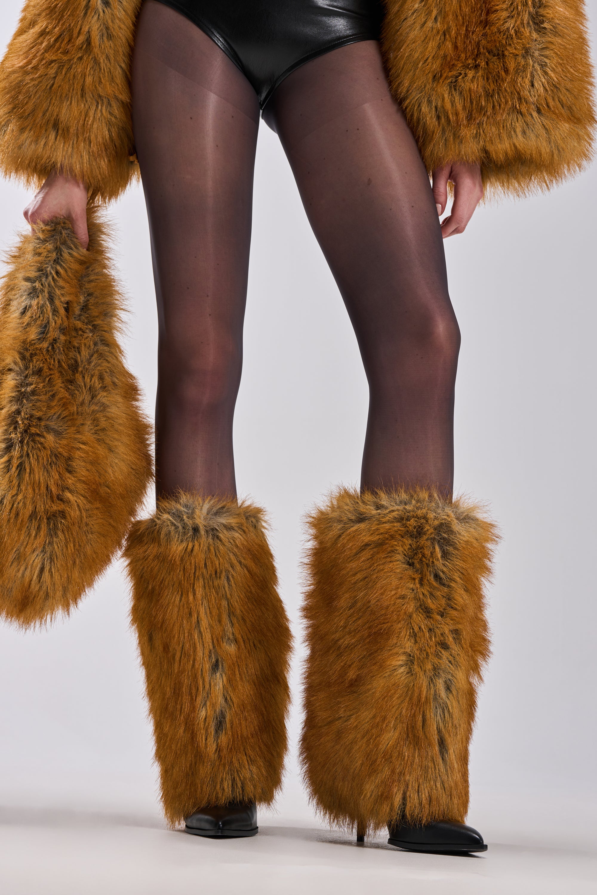 Wearing black shorts, sheer black tights, and AZALEA WANG EKKEN RED FOX FUR STILETTO BOOTS with large brown covers, the person holds a matching faux fur accessory. Only the lower body is visible.