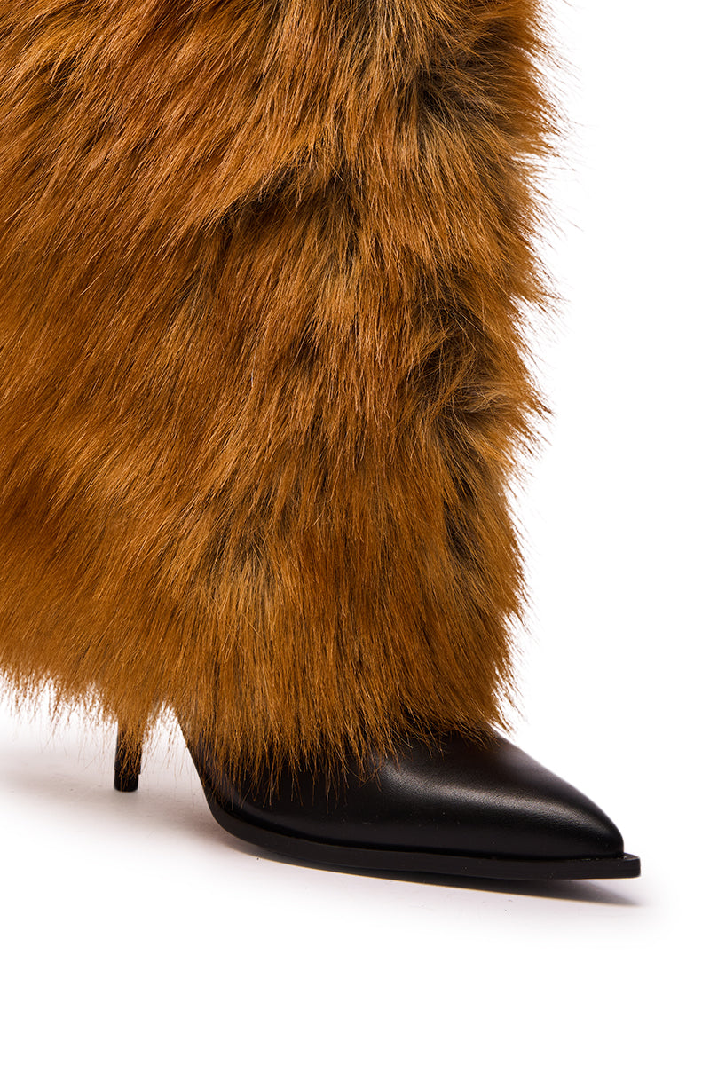 A close-up of the AZALEA WANG EKKEN RED FOX FUR STILETTO BOOT, featuring black faux fur, a pointed toe, and thin heel, partially covered by shaggy brown faux fur pants or leg warmers.