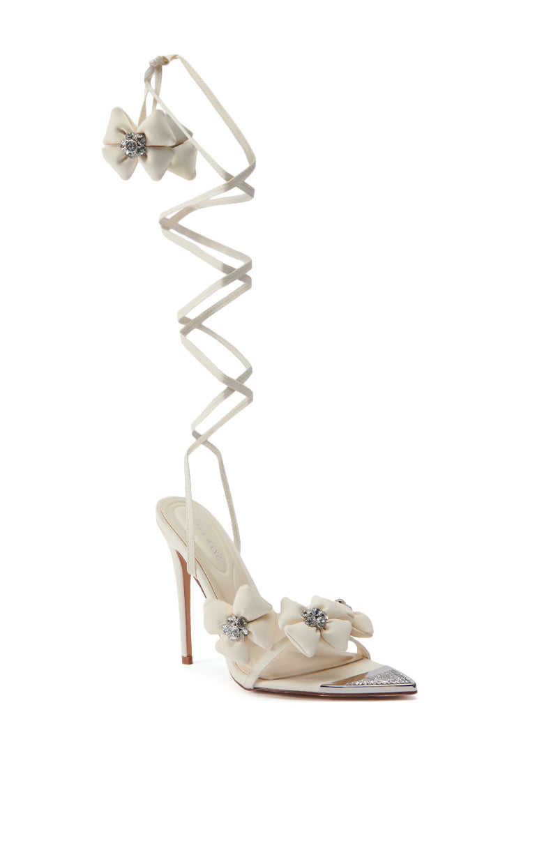 The AZALEA WANG ELAINE EMBELLISHED SANDAL IN TAN is a chic high-heeled faux leather sandal featuring a tan color with delicate ribbon detailing and silver embellishments. The open pointed toe design is complemented by an intricate ankle wrap with bow accents, while the stiletto heel is thin and elegant, perfect for formal or special occasions.
