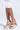 A person is wearing AZALEA WANG ELENAOR GOLD PEARL CHUNKY SANDALS with pearls, a faux leather upper, thick heels, and ankle straps. They're also in a white lace garment with ruffled trim against a plain light background.