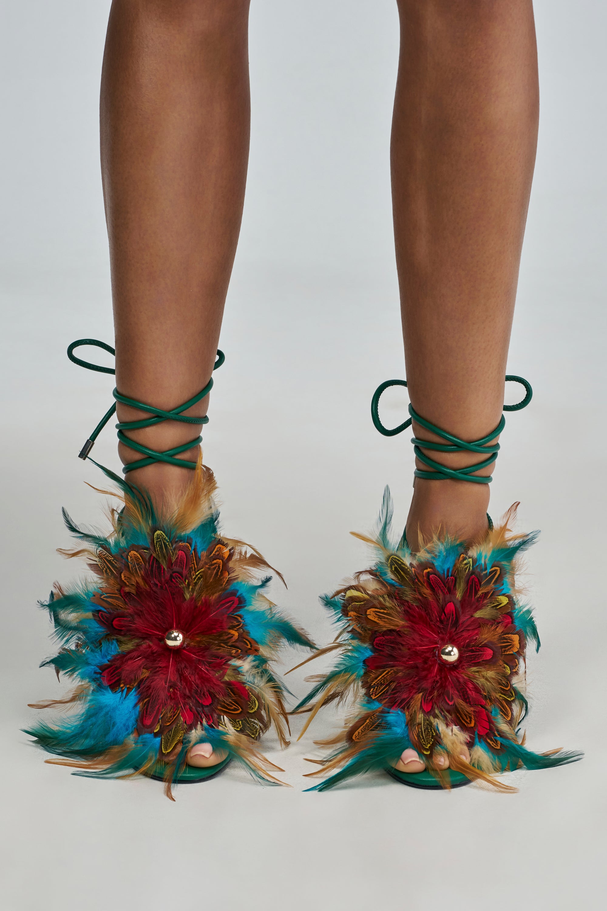 AKIRA GOLD ELFRIEDA GREEN BLOCK SANDAL: emerald green faux leather sandals with block heels, lace-up ankle ties, and large, multicolored feather flower embellishments on the toe straps.