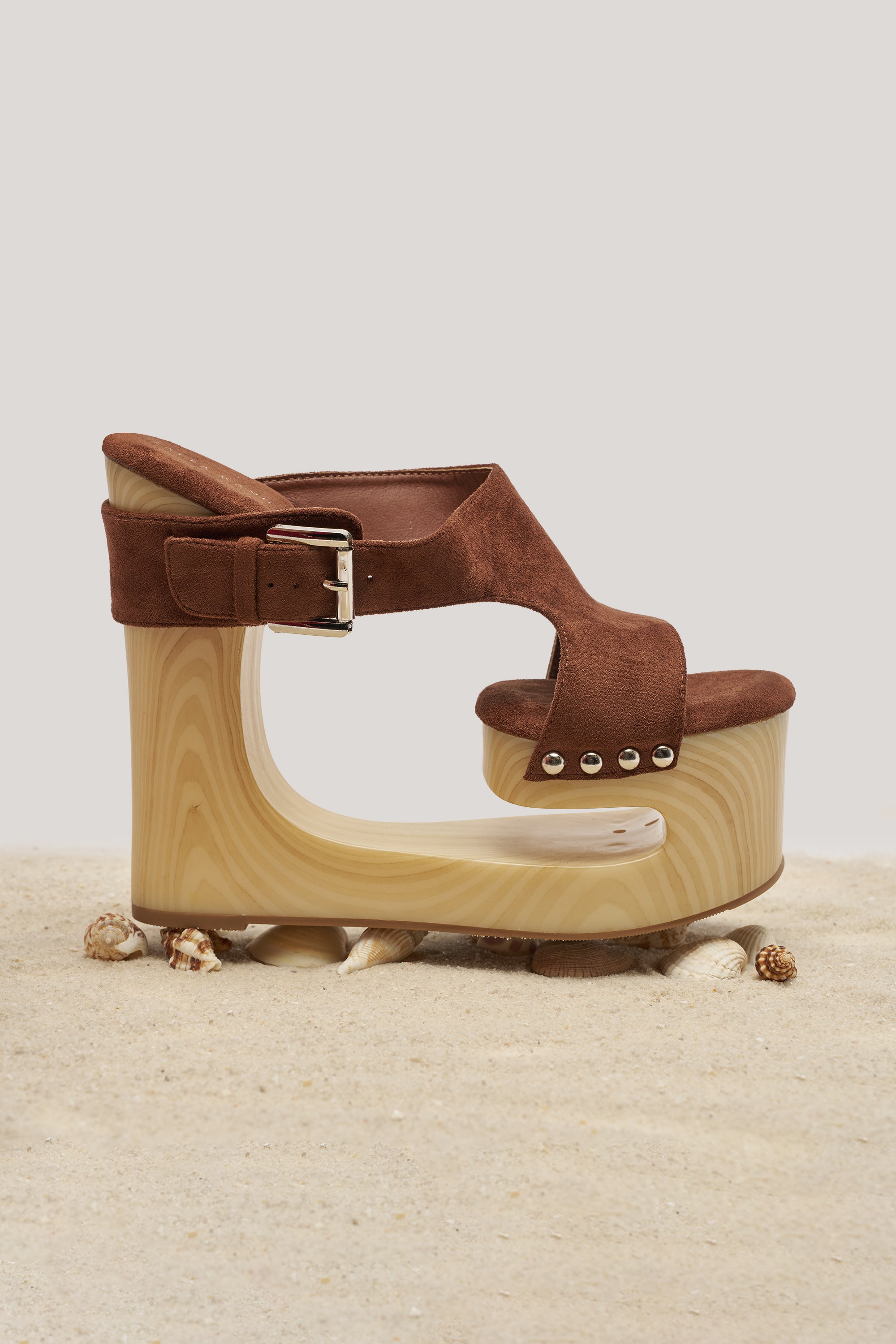 The AZALEA WANG ELGEDI TAN PLATFORM SANDAL features brown suede, a wooden cut-out wedge heel, and a metallic buckle—styled on sand with seashells for the ultimate boho-chic vibe. 1
