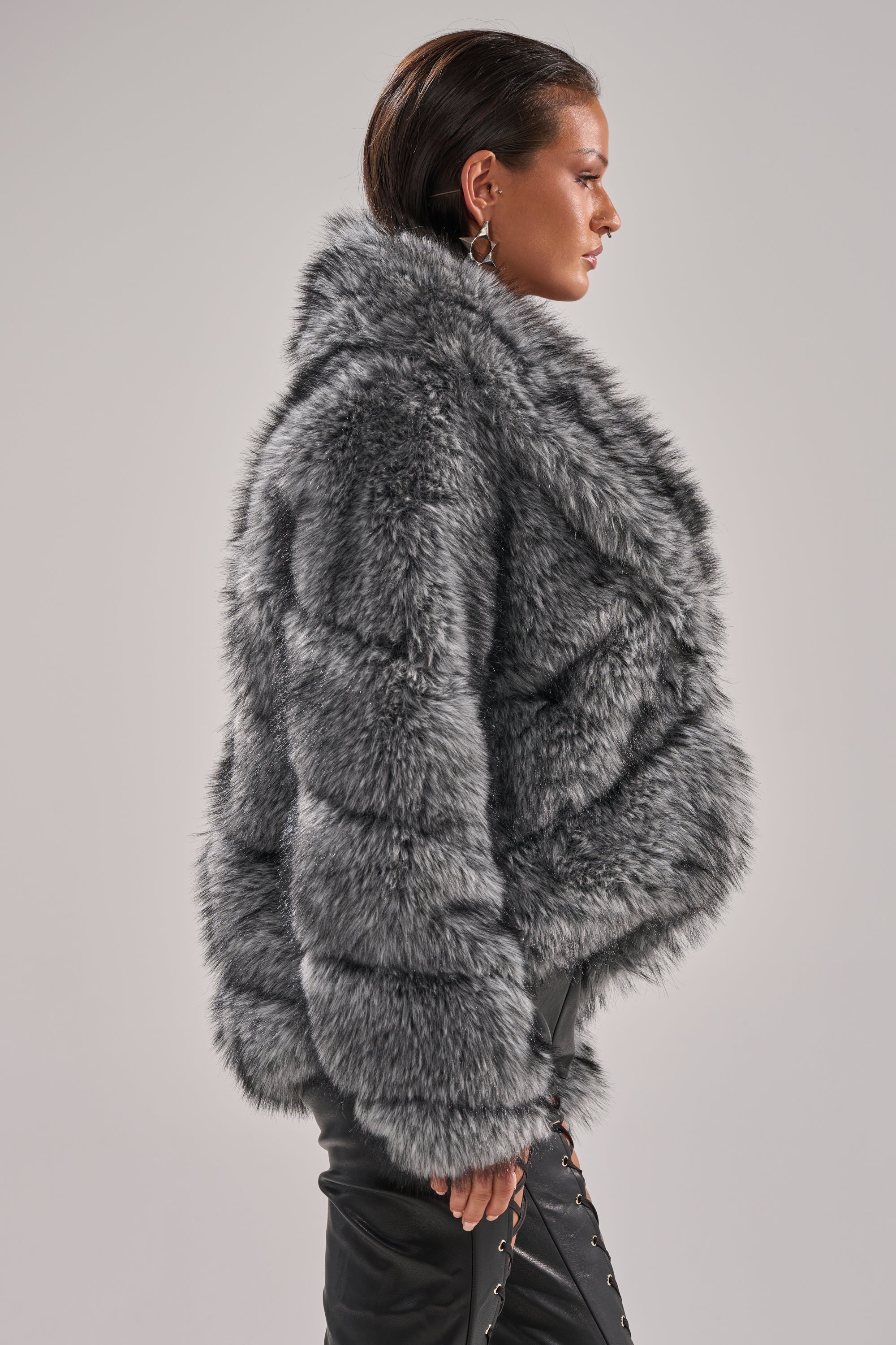 Wearing the ELIXIR PANELED FAUX FUR IN GREY, a person with slicked-back hair and black lace-up side pants stands in profile against a plain light gray background. 4