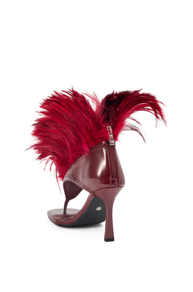The AKIRA Gold Elizaveta Burgundy Feather Thong Sandal features glossy faux patent leather, a stiletto heel, bold burgundy feathers at the heel, a back zipper closure, and is shown against a white background. 6