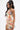 Wearing hoop earrings, a woman with long dark hair stands against a plain white background in the strapless FLOUNCE CORSET MINI DRESS. It features mixed print fabric, a lace-up front, and pleated skirt. She looks to the side.