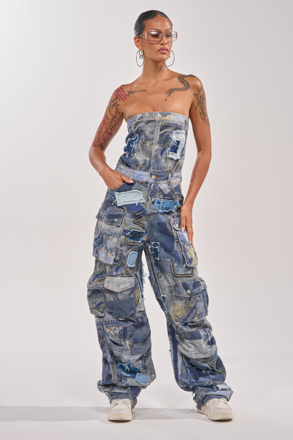 A person models the PATCHWORK DENIM ON DENIM JUMPSUIT—strapless, with multiple pockets—paired with white sneakers, confidently posing against a plain white background. 1