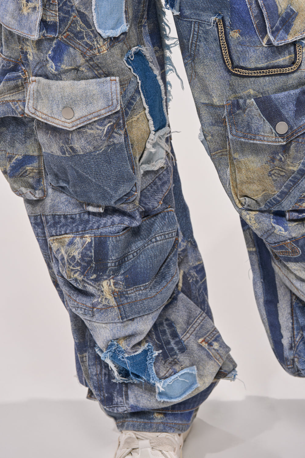 Close-up of a person wearing the PATCHWORK DENIM ON DENIM JUMPSUIT, featuring various blue denim shades, visible seams, frayed edges, and multiple pockets, paired with white shoes. 5