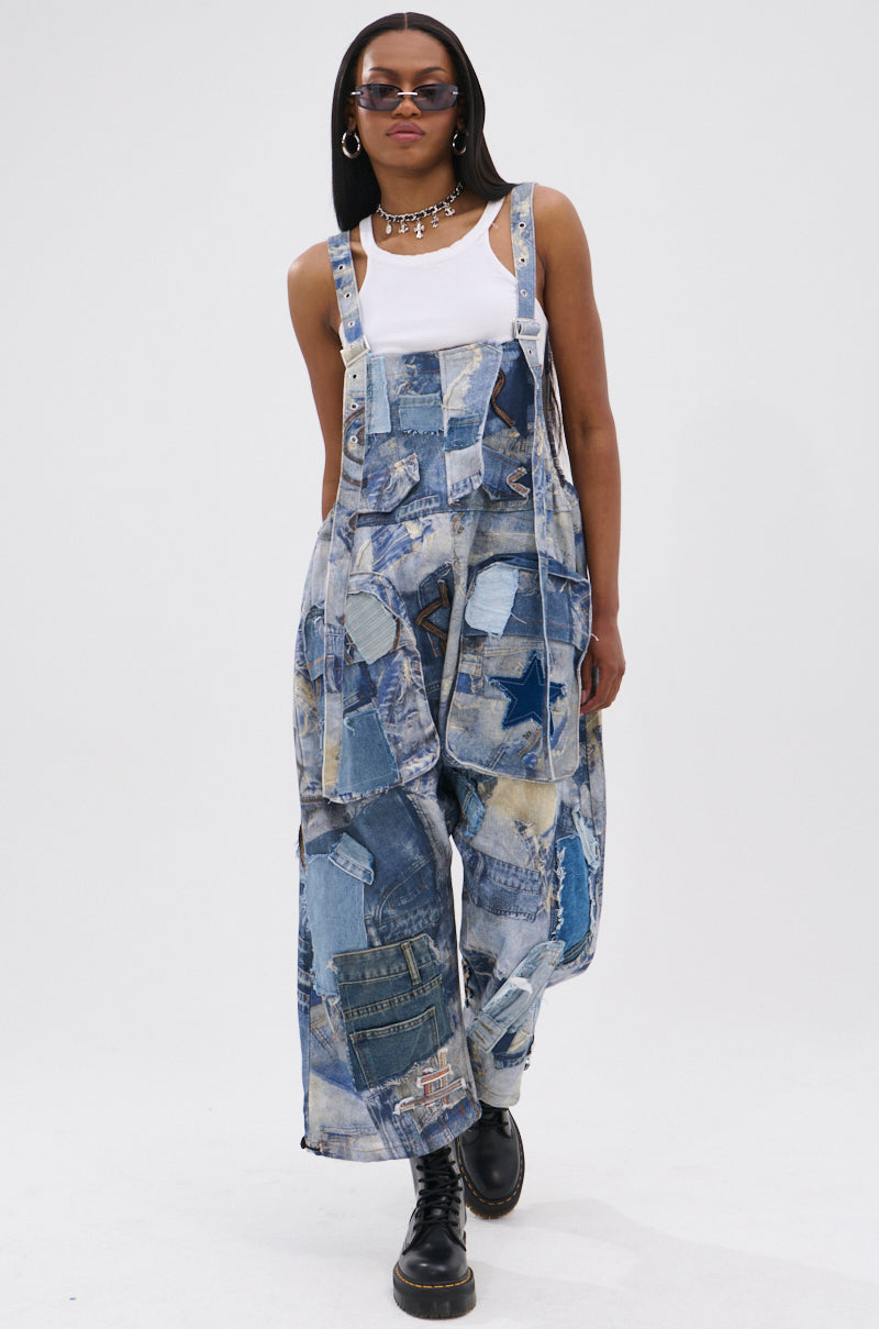 A person wears the FOR THE GRAM PATCHWORK OVERALLS—denim with adjustable straps and patchwork print—styled with a white tank top, chunky black boots, sunglasses, and a silver chain necklace against a plain white background.
