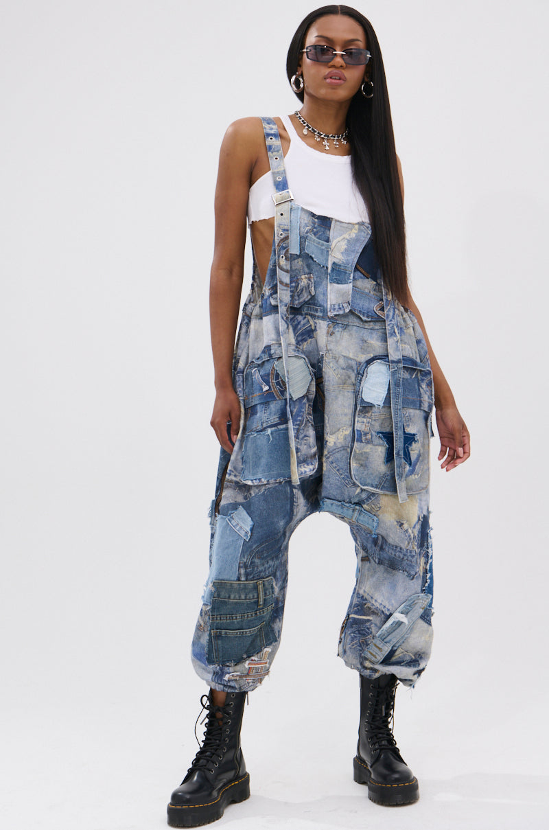Wearing the FOR THE GRAM PATCHWORK OVERALLS with adjustable straps, a white tank, black lace-up boots, sunglasses, and a chain necklace, a confident person stands against a plain light background.