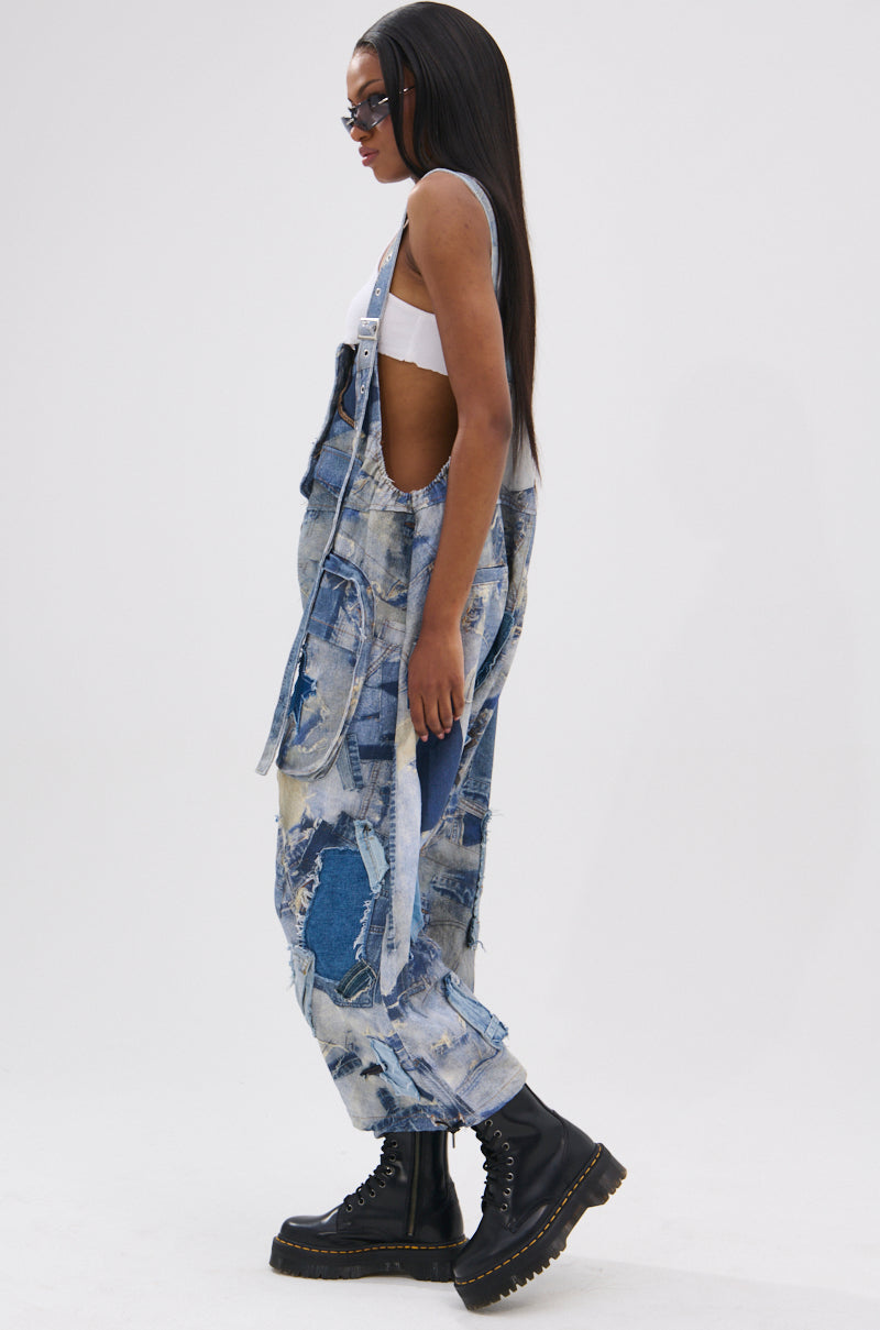 A person with long straight hair wears sunglasses, a white crop top, black platform boots, and FOR THE GRAM PATCHWORK OVERALLS with adjustable straps, standing in profile against a plain white background.
