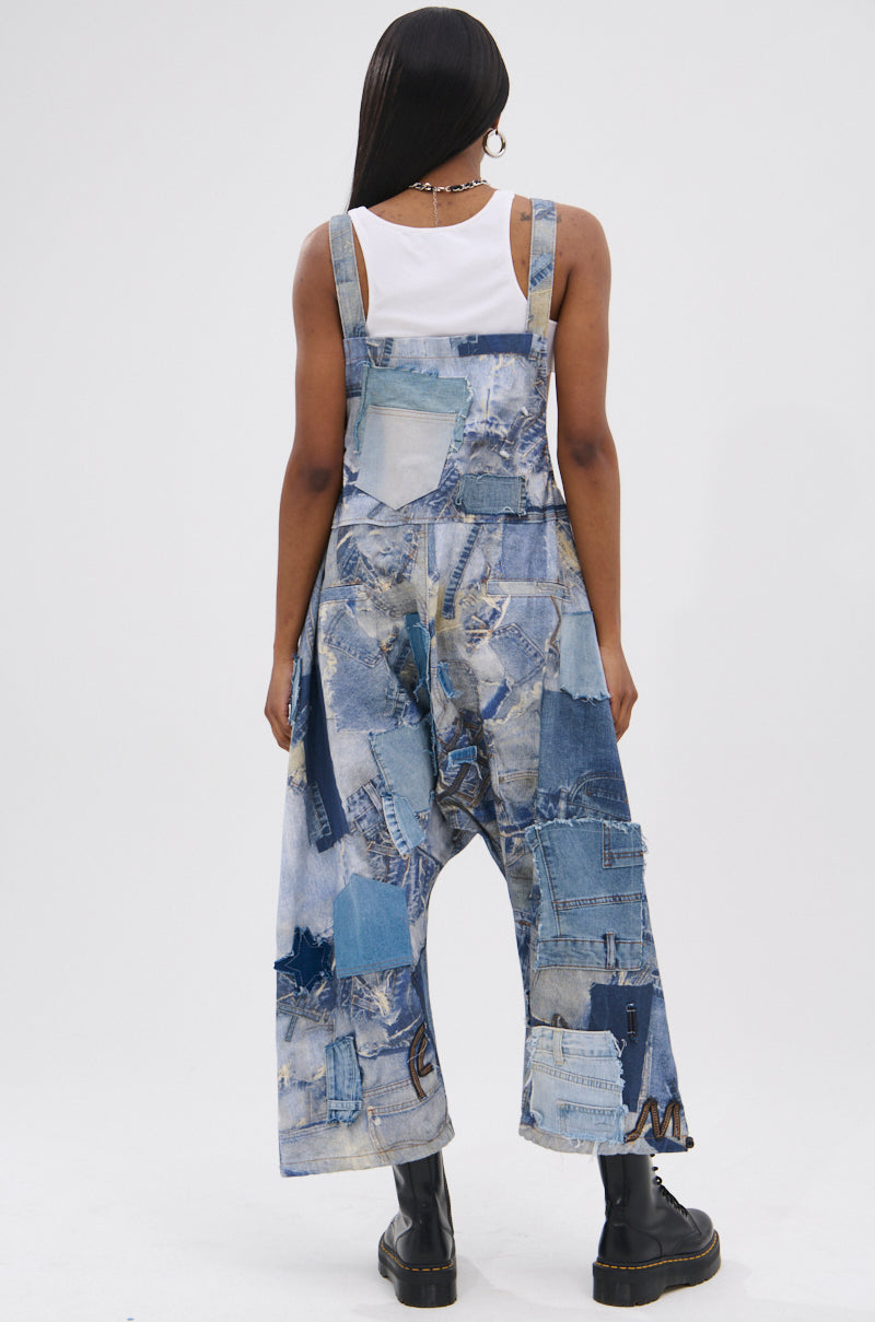 A person with long hair wears a white tank top and FOR THE GRAM PATCHWORK OVERALLS with adjustable straps, paired with black platform boots, standing against a plain light background.