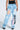 A person is seen from the back wearing FIRST CLASS TICKET GRAPHIC CARGO RELAXED LEG JEANS in light blue, featuring multiple pockets and graphic prints like text, a smiley face, and a heart, paired with a black top.