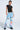 Wearing the FIRST CLASS TICKET GRAPHIC CARGO RELAXED LEG JEANS in light blue with bold, colorful prints and a black t-shirt, a person stands confidently against a plain white background.
